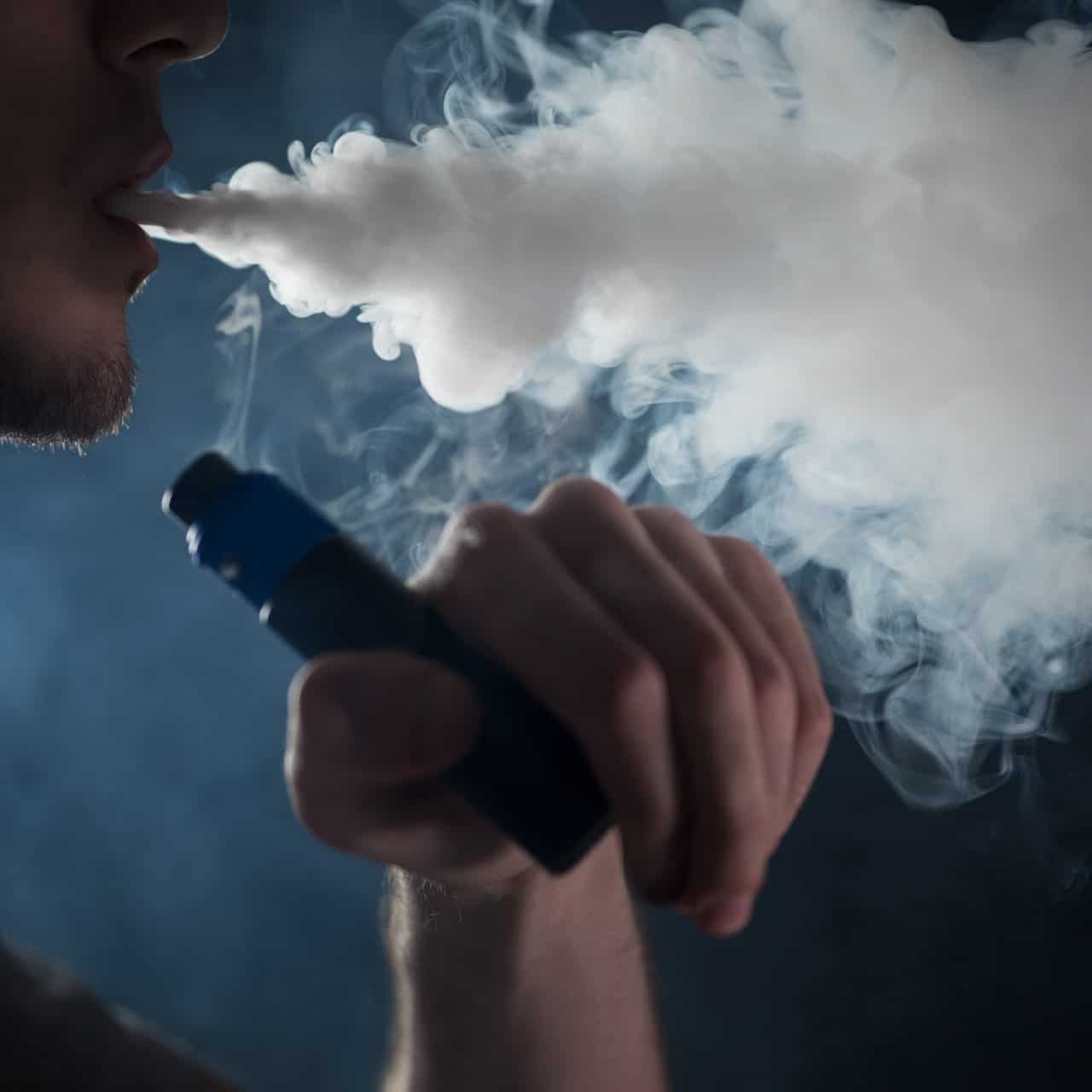Vape device emitting thick vapor, close-up of man vaping with e-cigarette, smoking, and vapor cloud.